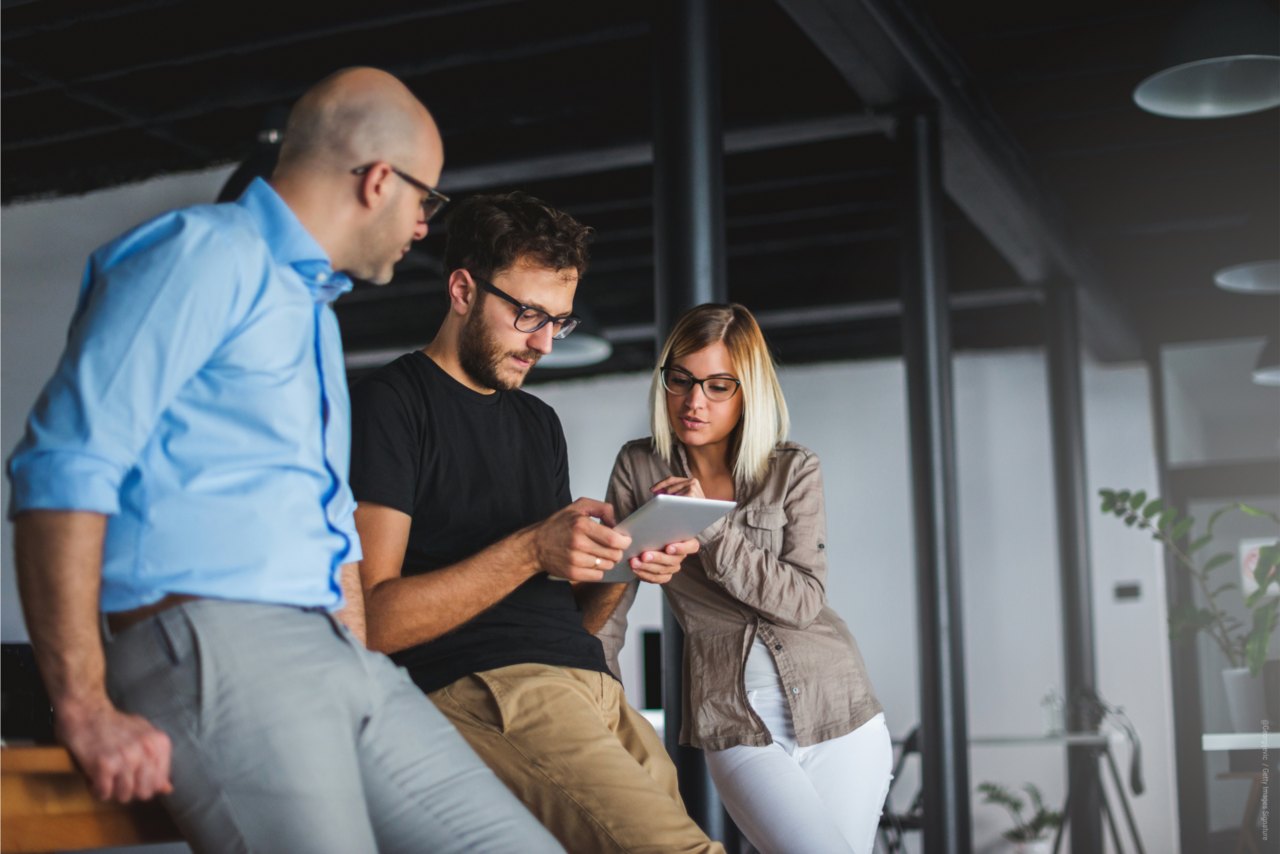 Junger Mann erklärt seinem Kollegen und seiner Kollegin etwas auf dem Tablet